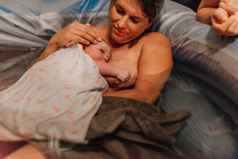 White mother holding newborn in birth pool